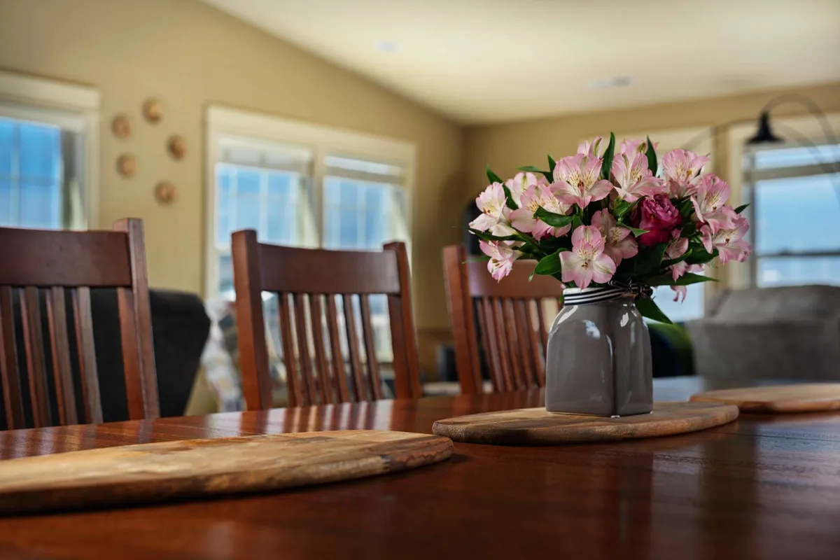 A beautifully set wooden dining table surrounded by matching chairs, accented with a fresh floral arrangement. The setting is primed for large group meals and celebrations, with a warm, welcoming atmosphere.