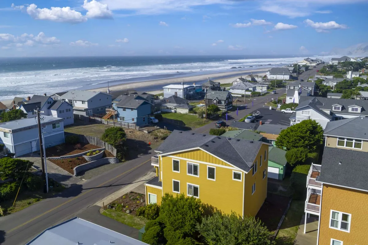 A relaxed exterior view featuring a cheerful yellow house with a striking ocean backdrop and a coastal road nearby. The setting hints at a laid-back coastal lifestyle, with easy access to both the beach and local community amenities.
