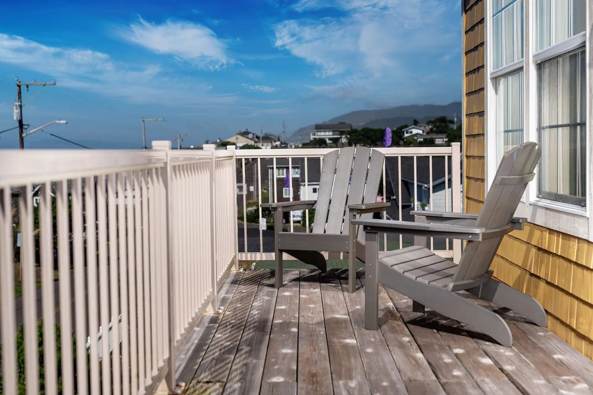 This image shows a peaceful balcony furnished with wooden chairs and a railing, offering a clear, unobstructed ocean view. The setting is serene and inviting, perfect for relaxing or enjoying a drink while taking in the sights and sounds of the coast.