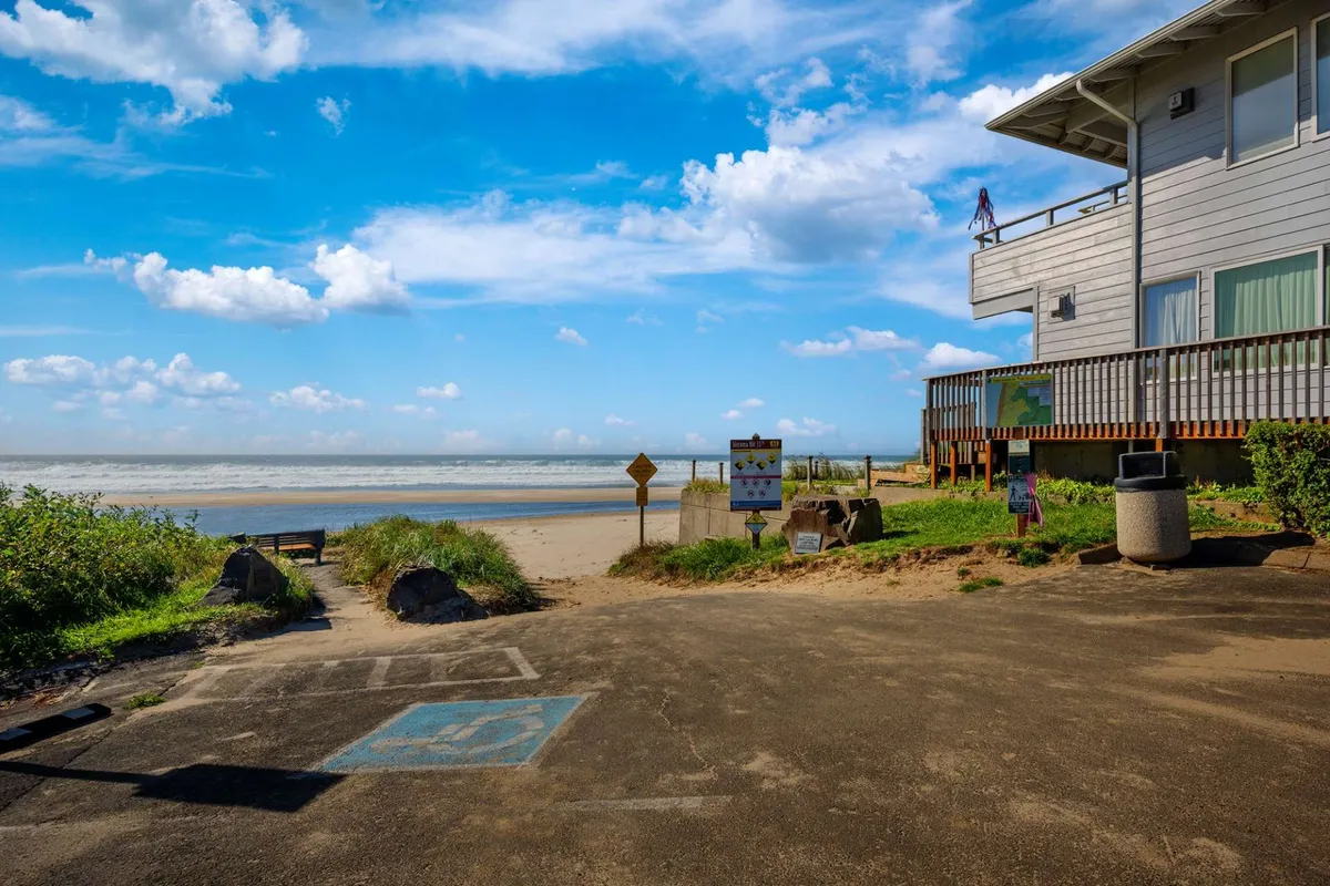 An exterior perspective showing a deck area overlooking the ocean, with clear signs pointing the way to beach access. The mood is calm and inviting, suggesting easy access from the home to the shoreline, with opportunities for relaxing and watching sunrises or taking evening strolls.