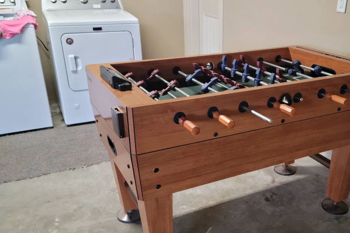 A fun and relaxed indoor scene featuring a foosball table next to a washing machine, creating a casual space for playful family bonding and leisure activities.
