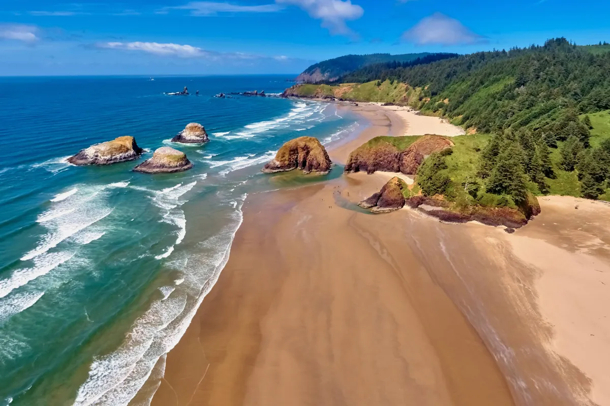 A scenic exterior view showcasing sandy beaches, dramatic rock formations, green hills, and gentle ocean waves—an inviting and natural space ideal for children to play and families to explore together.