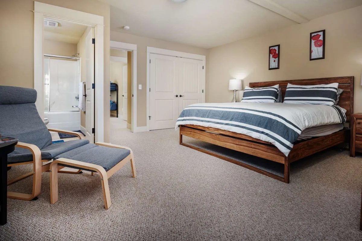 A serene bedroom featuring a comfortable bed with plush bedding, an armchair tucked into the corner for quiet reading, and calming artwork adorning the walls. Soft natural light enters the room, creating a tranquil and restful atmosphere ideal for unwinding.